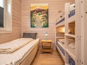 Quarto compacto com cama beliche, uma cama de solteiro e mesa de cabeceira com abajur.