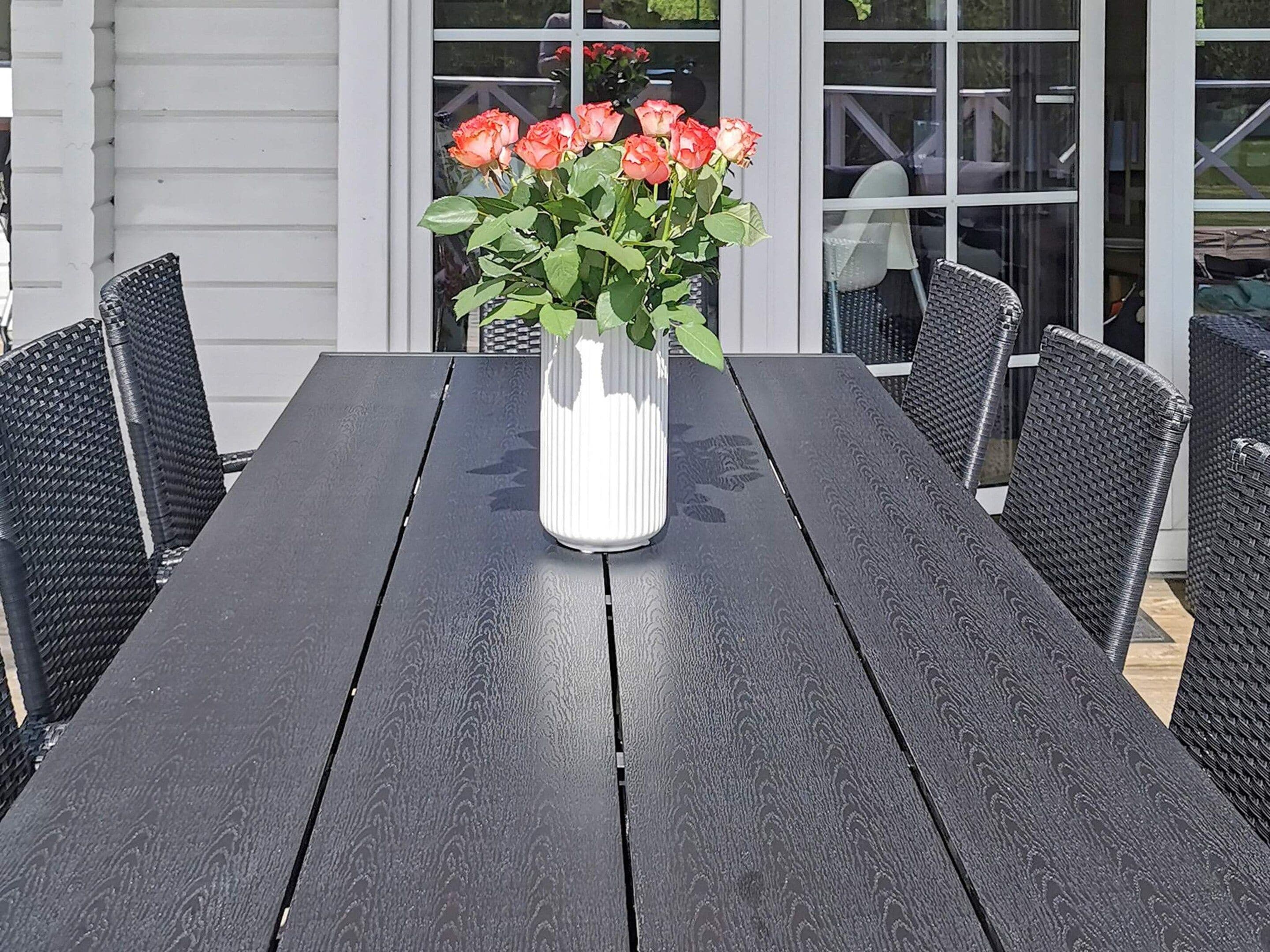 A table with a vase of flowers and wicker chairs.