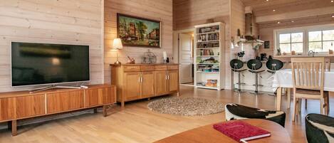 Amplia sala de estar con piso de madera, televisor, estantería y comedor con mesa y sillas.