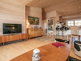 Amplia sala de estar con piso de madera, televisor, estantería y comedor con mesa y sillas.