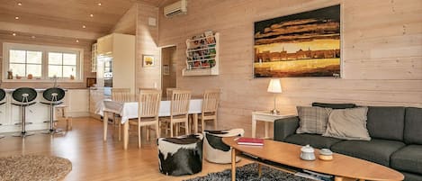 A spacious living area with a wooden ceiling, a dining table with chairs, a sofa, and a painting on the wall.