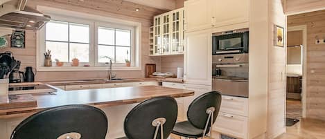 A modern kitchen with wooden floors, white cabinetry, a central island with bar stools, and a large window providing natural light.