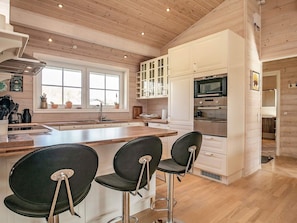 Cozinha moderna com piso de madeira, armários brancos, uma ilha central com banquetas e uma janela ampla que traz luz natural.