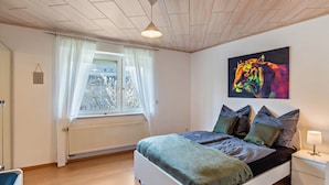 A bedroom with a bed, a window with curtains, a radiator, a nightstand, and a wall-mounted painting. - Apartment "Am Hirnach 2" with Shared Garden & Wi-Fi (Sindelfingen)