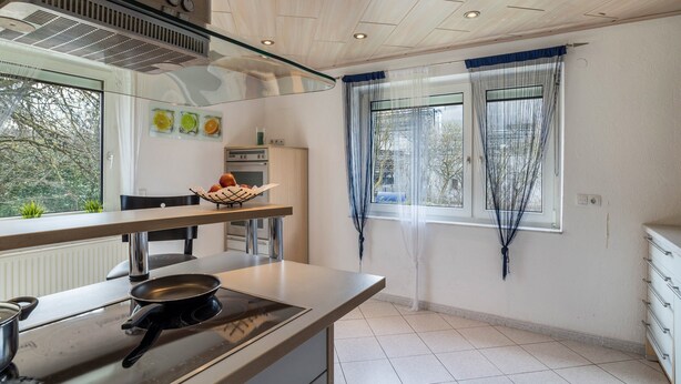 A modern kitchen with a stove, a dining table, and a window with curtains. - Apartment "Am Hirnach 2" with Shared Garden & Wi-Fi (Sindelfingen)