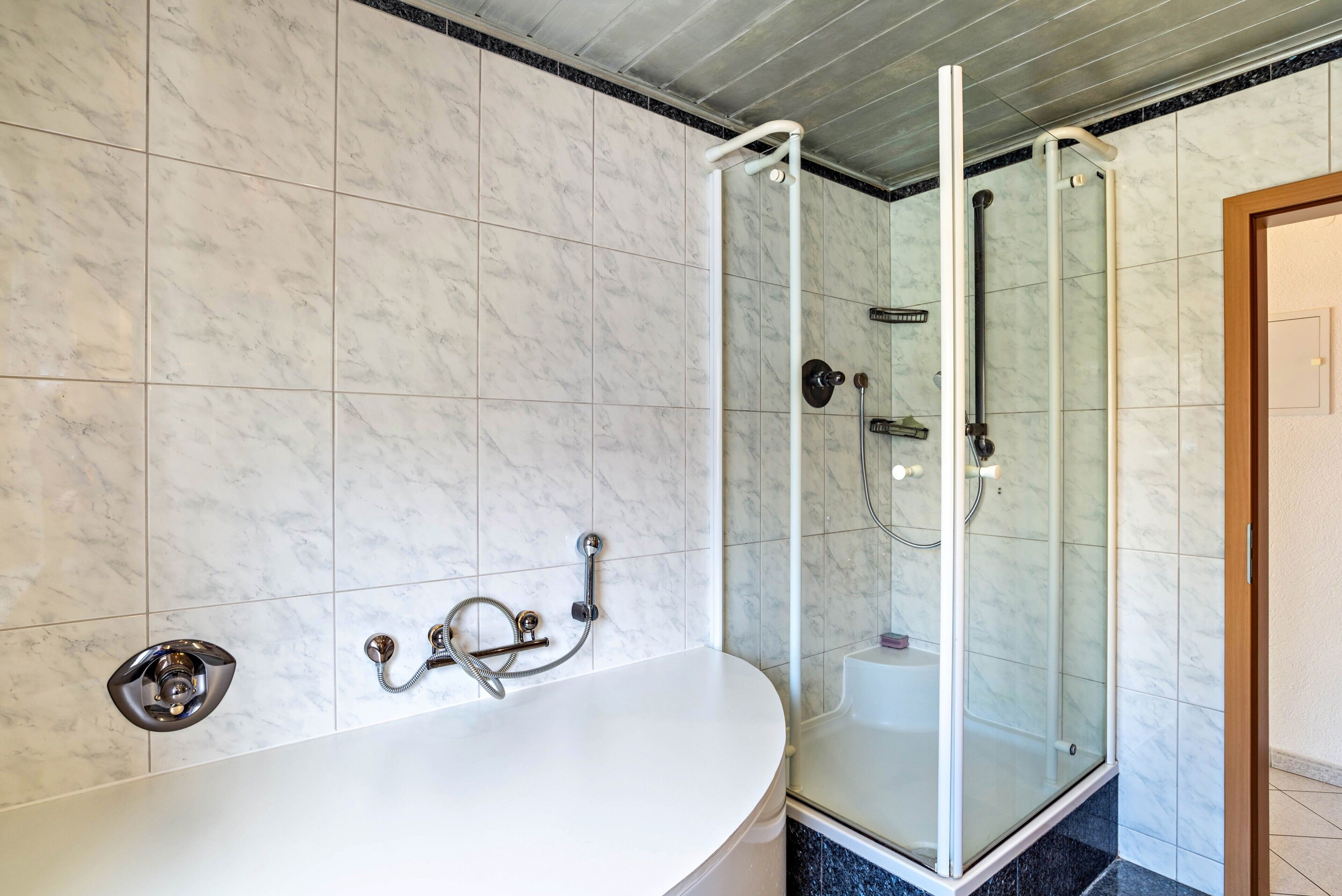 Ein Badezimmer mit einer freistehenden Badewanne, einer Duschkabine aus Glas und einer Wand mit Marmorfliesen.