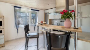 A modern kitchen with a dining area, a large window with curtains, and a vase with flowers on the counter. - Apartment "Am Hirnach 2" with Shared Garden & Wi-Fi (Sindelfingen)