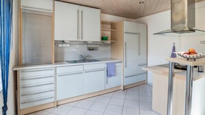 A modern kitchen with white cabinets, a stainless steel range hood, and a small island with a bowl of fruit. - Apartment "Am Hirnach 2" with Shared Garden & Wi-Fi (Sindelfingen)