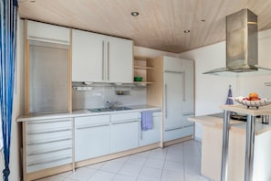 Une cuisine moderne avec des armoires blanches, une hotte en acier inoxydable et un petit îlot central sur lequel se trouve un panier de fruits.