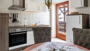 A kitchen with a stove, oven, and hanging utensils; a dining area with a table and chairs; and a wooden door leading outside.