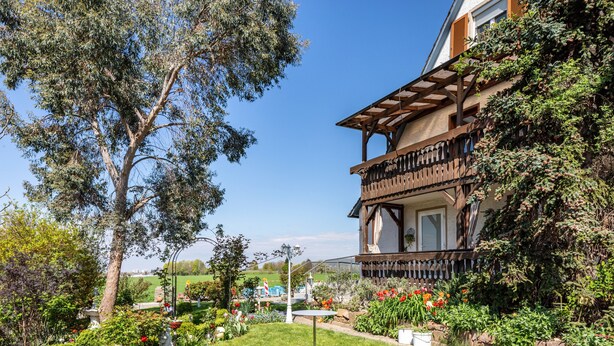 A two-story building with a balcony, surrounded by a well-maintained garden with various plants and flowers.