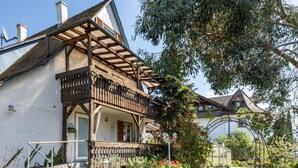 A traditional building with a balcony, a garden with flowers, and a clear sky.