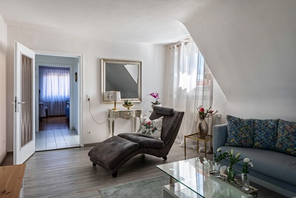 Una sala moderna con un sofá, un sillón reclinable, una mesa de centro de vidrio y una mesita auxiliar con adornos.