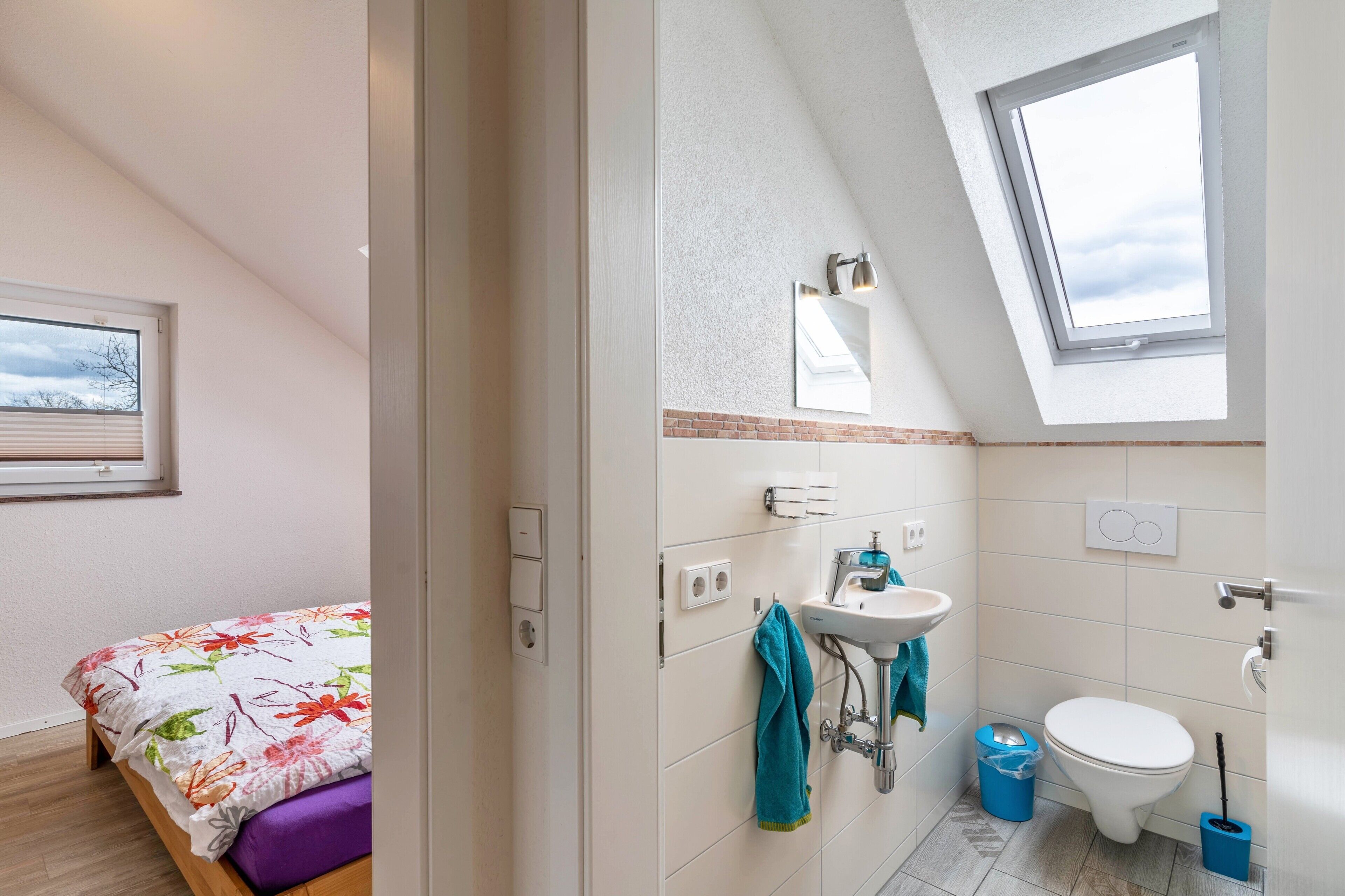 Een slaapkamer met een bed, dakraam, badkamer met wastafel, toilet en een raam.