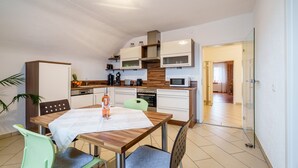 Eine moderne Küche mit weißen Schränken, einem Holztisch und einer Glastür zu einem Flur.