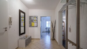Ein Flur mit weißer Wand, einer Wandtafel mit Muster, einem kleinen Konsolentisch und einer Tür mit Handtuchhalter.