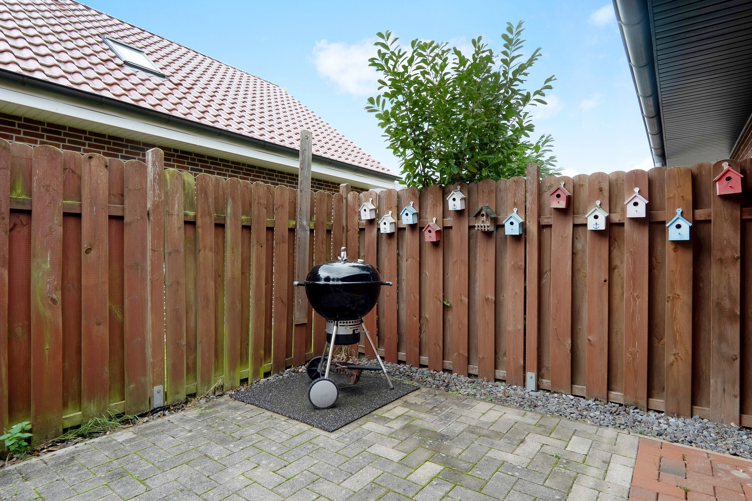A backyard with a barbecue grill, a wooden fence, and birdhouse decorations.