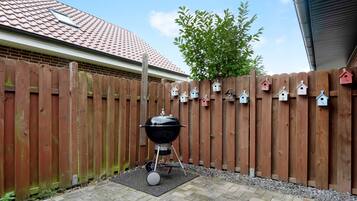 A backyard with a barbecue grill, a wooden fence, and birdhouse decorations.