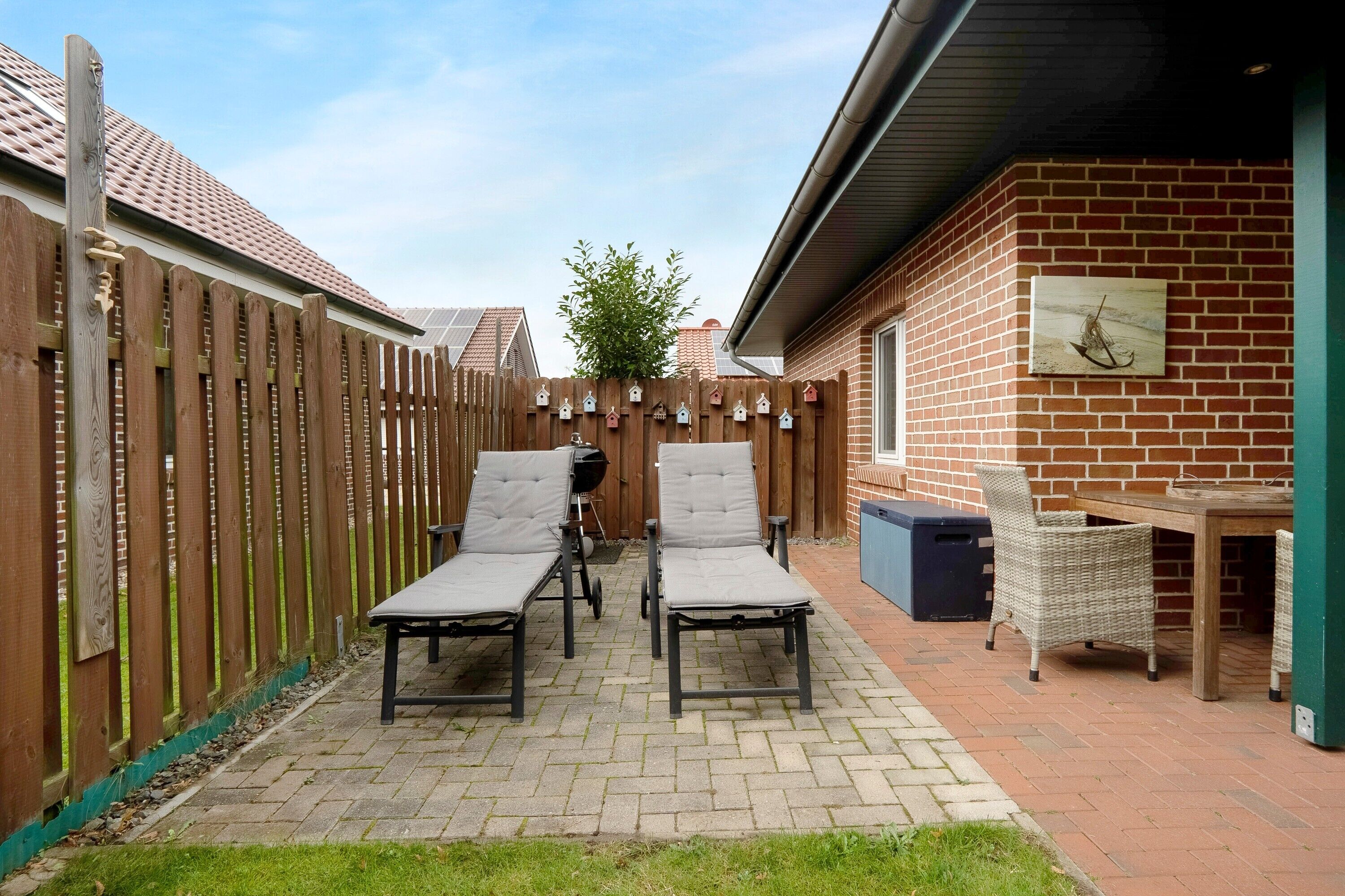 Eine Terrasse mit zwei Liegestühlen, einem Grill und einer Ziegelwand mit einem Bild.