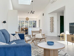 Una sala de estar moderna con un sofá azul, sillas de mimbre, una mesa de centro redonda y una televisión.