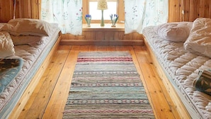A cozy cabin room with two beds, a wooden floor, floral curtains, and a window with a lamp. - 4 Person Holiday Home in Tallberg-by Traum (Tallberg)