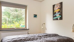 A bedroom with a bed, a window with a view of greenery, a wall-mounted lamp, and a painting. - 8 Person Holiday Home in Struer (Struer)