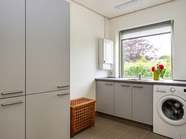 Un lavadero pequeño con lavadora, una cesta de madera y una ventana con vistas a la vegetación.