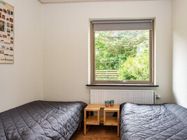 Un dormitorio con dos camas individuales, una mesita de madera, un ventanal con vistas a la vegetación y un radiador abajo.