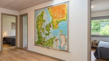 Ein Zimmer mit einer großen Karte an der Wand, Holzdielen und einem Bett mit grauer Bettdecke.