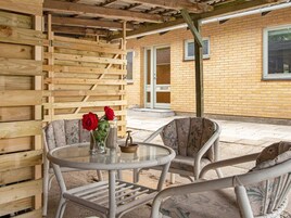 An outdoor seating area with a round table and two chairs, a wooden wall, and a brick building in the background.