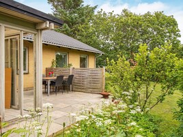 A house with a patio, a table, and chairs, surrounded by greenery and trees.