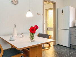A dining area with a table, chairs, a vase with red roses, a clock, and a refrigerator.