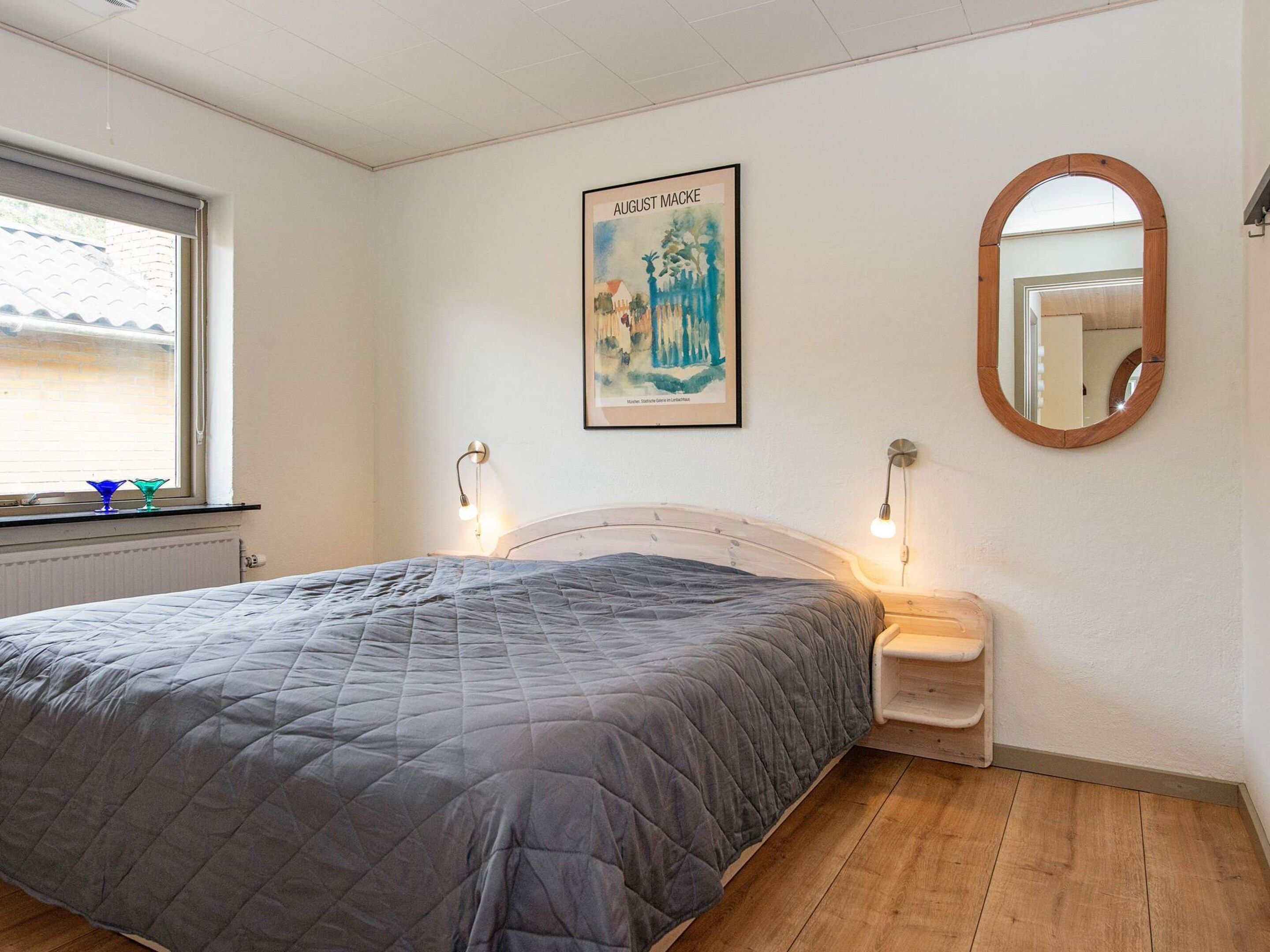 A bedroom with a bed, a window, a painting, a mirror, and bedside lamps.