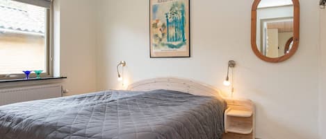 A bedroom with a bed, a window, a painting, a mirror, and bedside lamps.