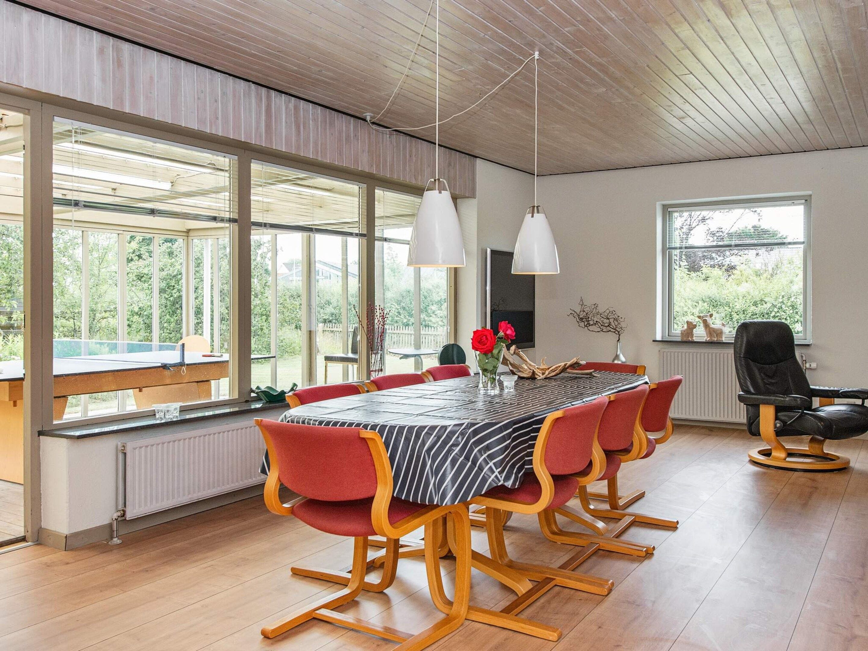 A dining area with a long table, red chairs, and pendant lighting.