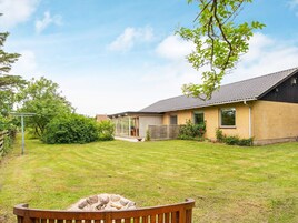 A residential property with a well-maintained lawn, a wooden bench, a fire pit, and a house with a sloped roof and brick exterior.