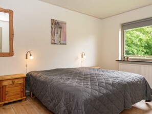 A bedroom with a bed, bedside lamps, a wooden nightstand, a painting on the wall, and a window with a view of trees. - 8 Person Holiday Home in Struer (Struer)