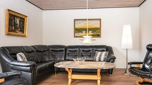 A living room with a black leather sectional sofa, a round coffee table, and a painting on the wall. - 8 Person Holiday Home in Struer (Struer)