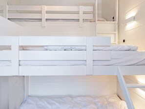 Une chambre avec un lit superposé, dotée de linge de lit blanc et d’une tête de lit.