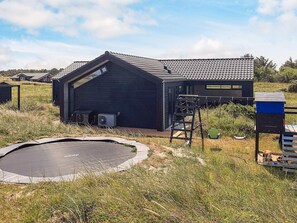 Un bâtiment moderne doté d’un toit en pente, d’un petit espace extérieur avec un trampoline et d’une échelle menant à une fenêtre.