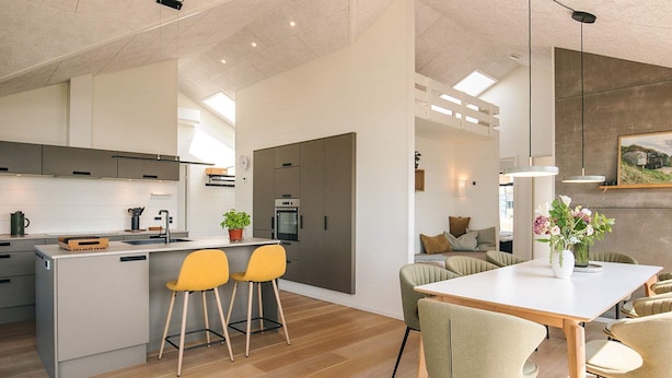 A modern kitchen with a central island, bar stools, and a dining area with a table and chairs. - 8 Person Holiday Home in Hirtshals (Hirtshals)