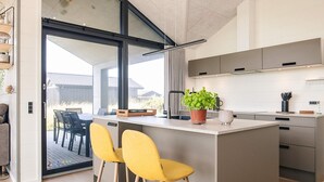A modern kitchen with a central island, bar stools, and a potted plant. - 8 Person Holiday Home in Hirtshals (Hirtshals)