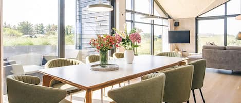 Uma área de jantar moderna com uma mesa comprida, várias cadeiras e um vaso de flores.