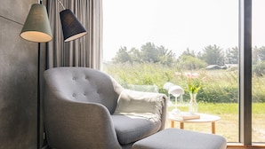 A modern room with a grey armchair and ottoman, a floor lamp, and a view of greenery outside. - 8 Person Holiday Home in Hirtshals (Hirtshals)