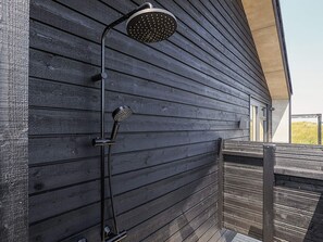 Una ducha exterior moderna adosada a una terraza de madera.