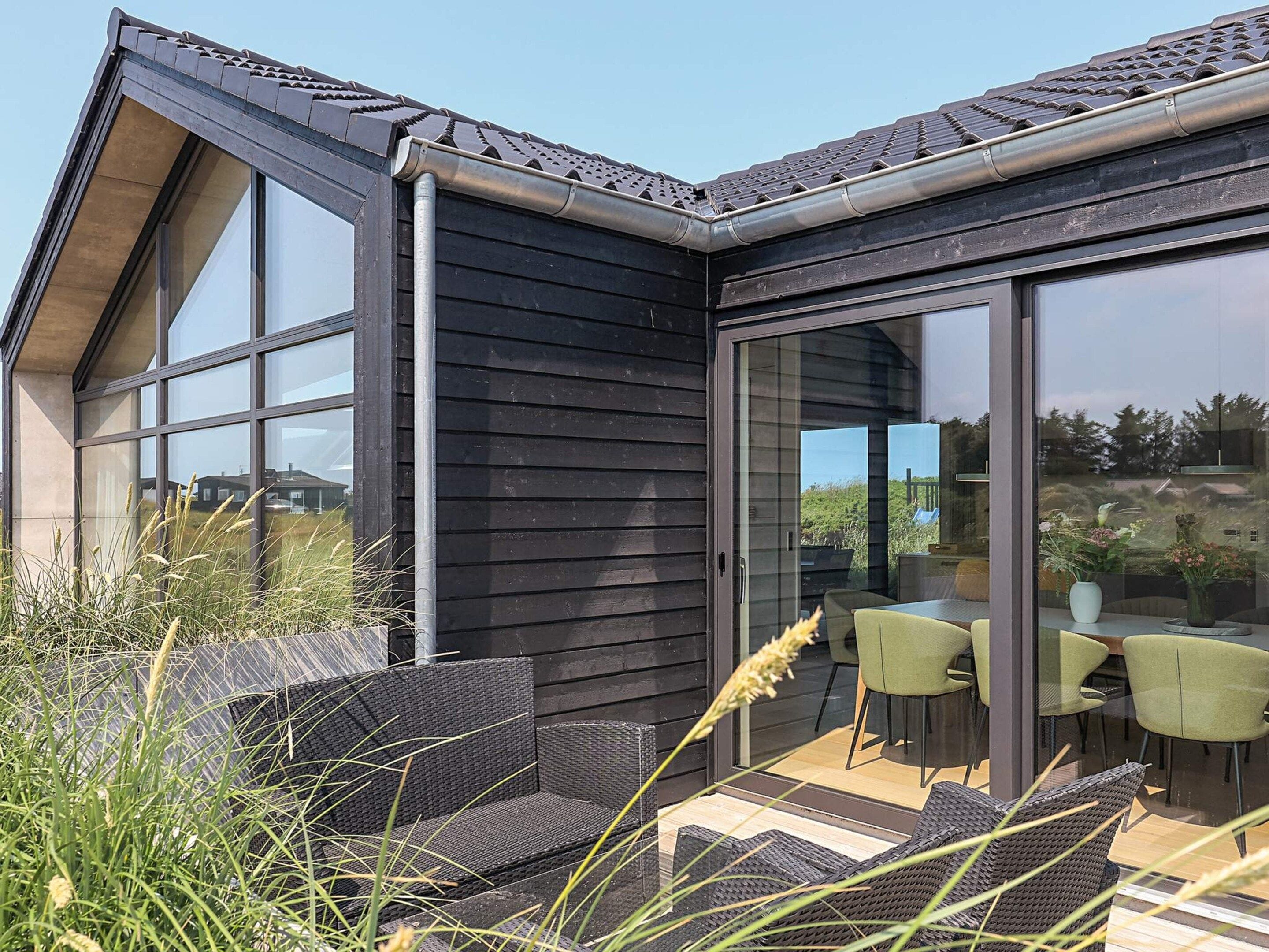 Een modern huis met een grote glazen deur die leidt naar een terras met rieten meubels.