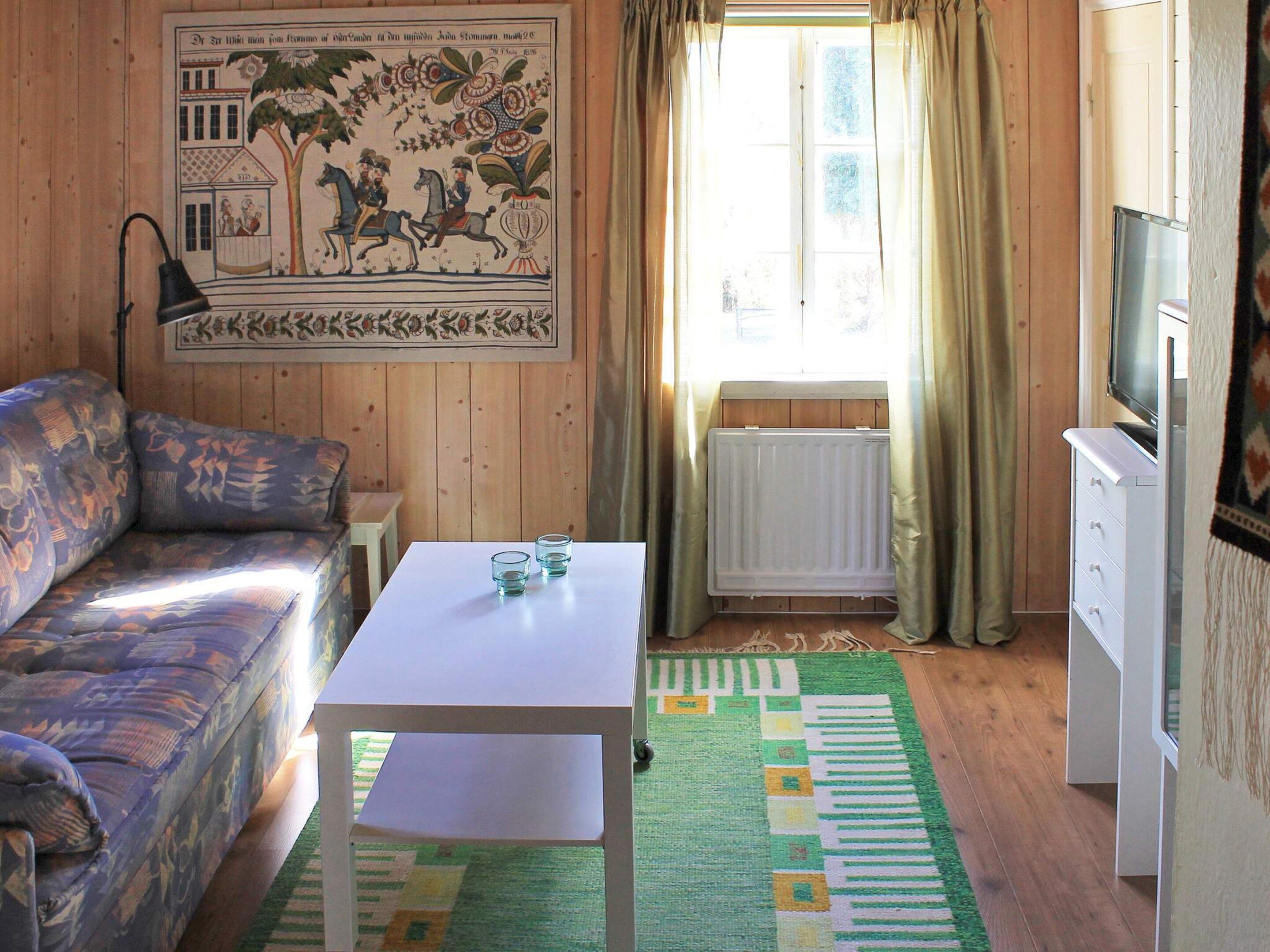 A room with a sofa, a small table, a radiator, a television, and a window with curtains.