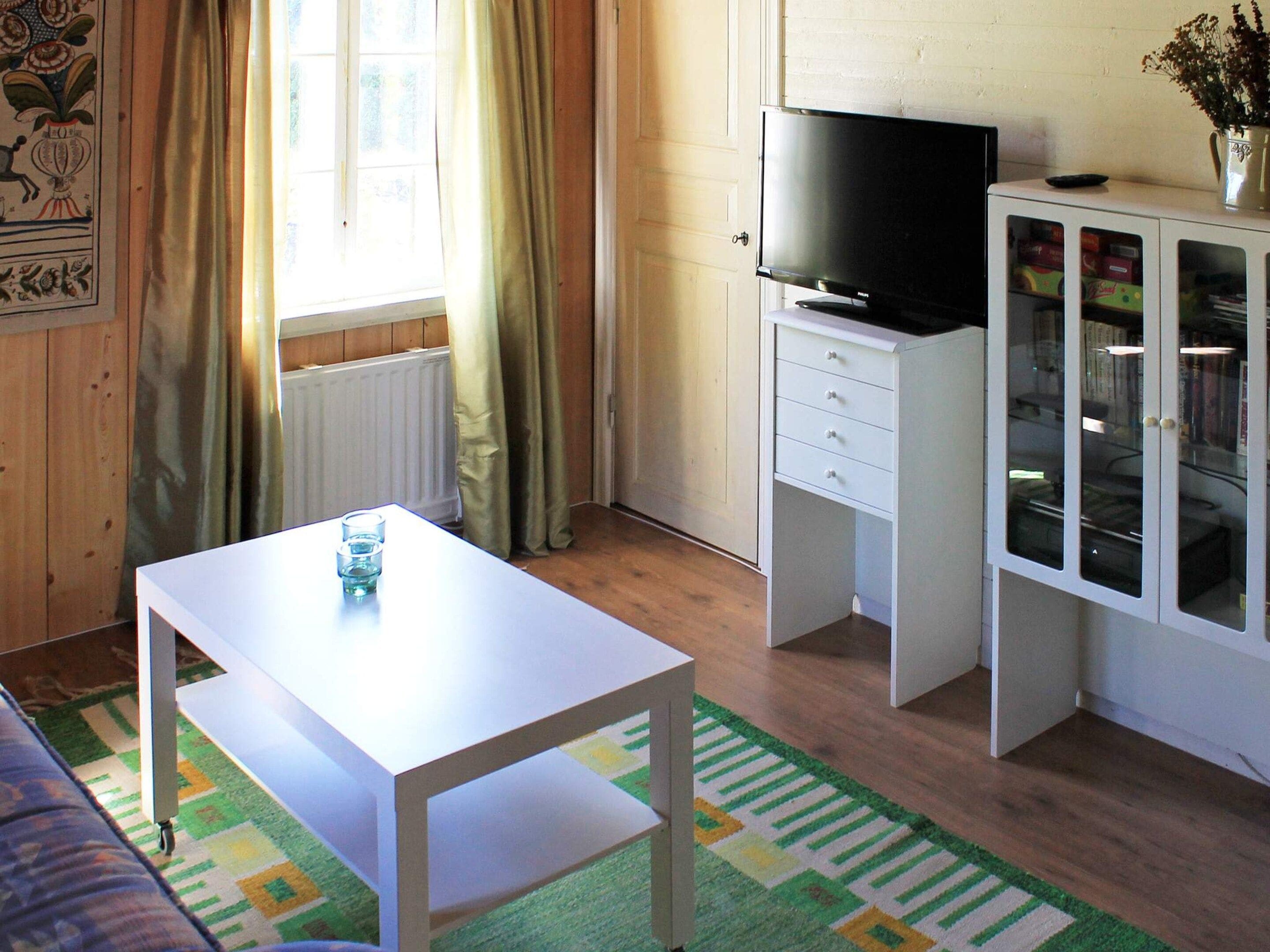 A room with a white table, a television on a cabinet, and a cabinet with glass doors.