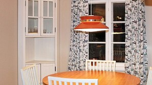 A dining area with a round wooden table, white chairs, a hanging pendant light, and a window with patterned curtains. - 6 Person Holiday Home in Stjarnhov (Stjarnhov)