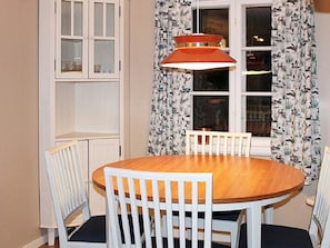 A dining area with a round wooden table, white chairs, a hanging pendant light, and a window with patterned curtains. - 6 Person Holiday Home in Stjarnhov (Stjarnhov)
